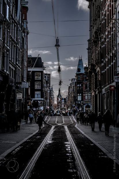 A street in Amsterdam, wet tram rails running into the distance between tall canal houses