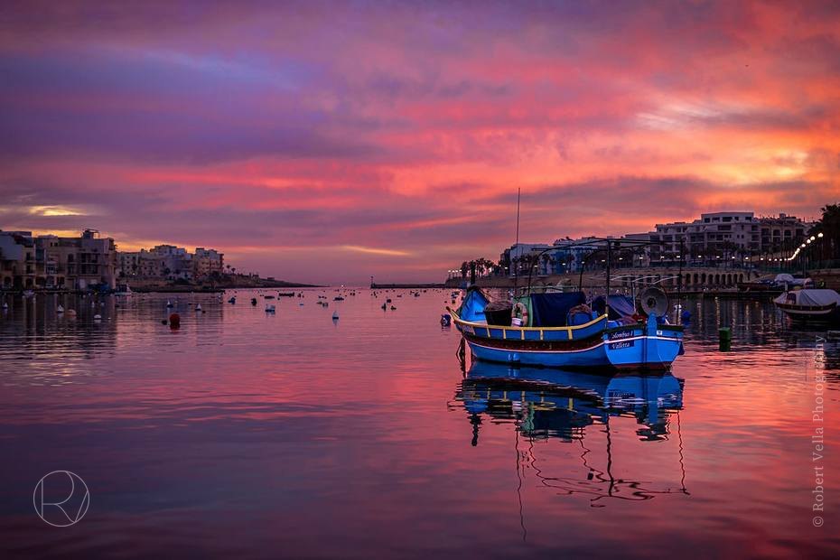 Fishing boats moored in a harbour at sunset, the whole sky and water turned pink
