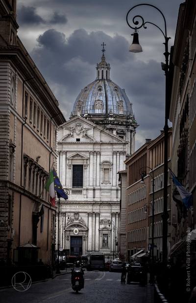 A baroque church dome at the end of a narrow street in Rome, a scooter parked below