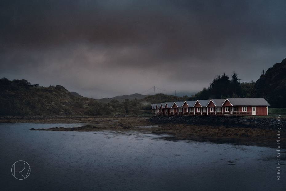Red boathouses along a fjord shore under a heavy sky