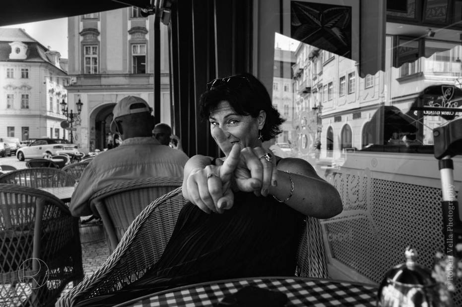 A woman at a café table pointing straight at the camera, black and white