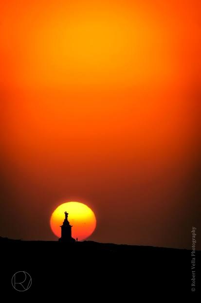 A huge orange sun going down behind a figure on a ridge