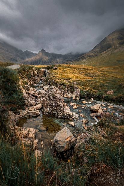 A rocky stream in a highland valley, mist sitting on the slopes above