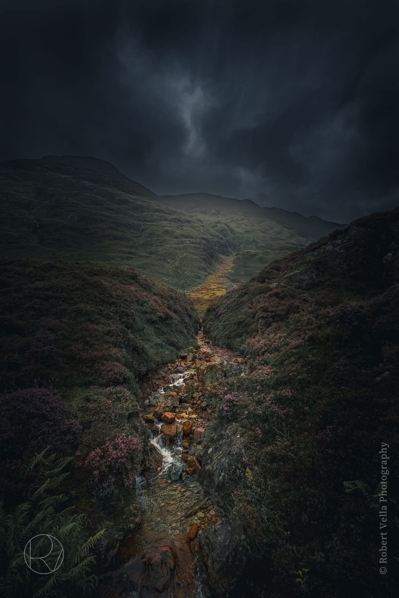 A steep glen seen from above, a stream threading down through it under heavy cloud