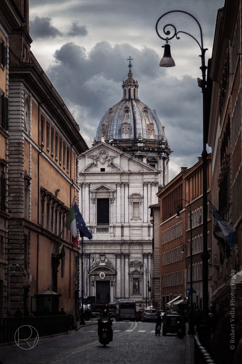 A baroque church dome at the end of a narrow street in Rome, a scooter parked below